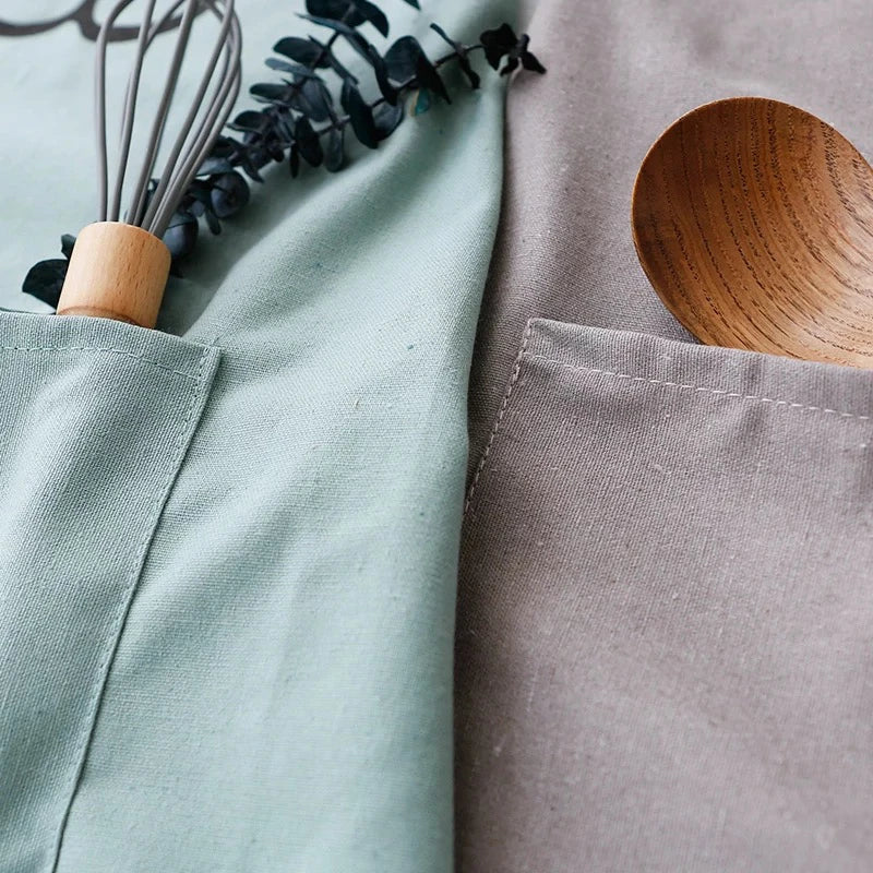 Close-up of green and gray apron pockets holding a whisk and wooden spoon
