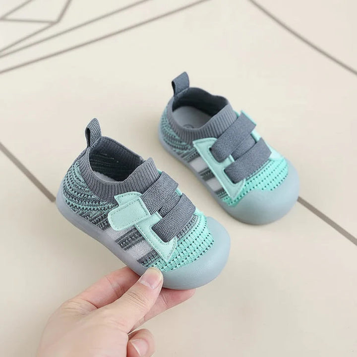 Green baby shoes with gray mesh uppers and double straps displayed on a tiled floor