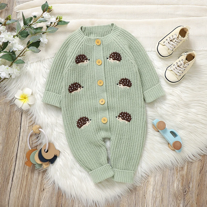 Green hedgehog baby jumpsuit laid flat beside shoes and flowers.