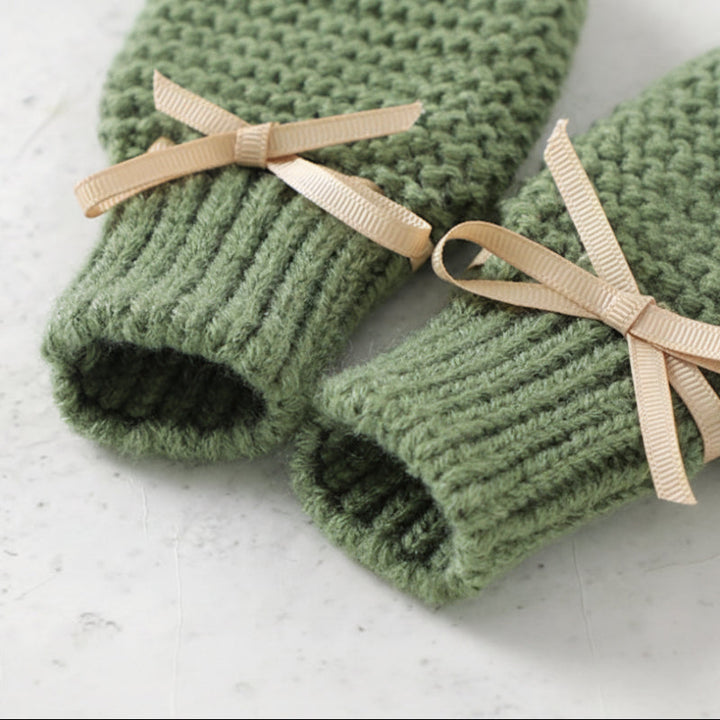 Green knitted mittens showing ribbed cuffs and beige ribbon bows