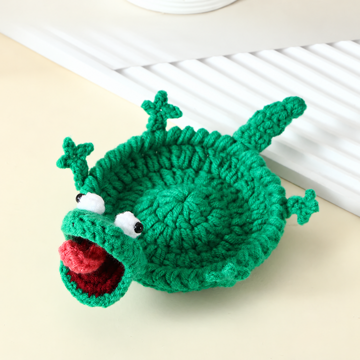 Green crocheted lizard coaster with a long tail, raised eyes, and an open mouth