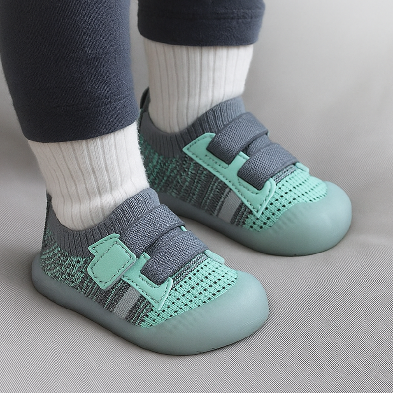 Green mesh baby shoes with gray straps worn with white socks