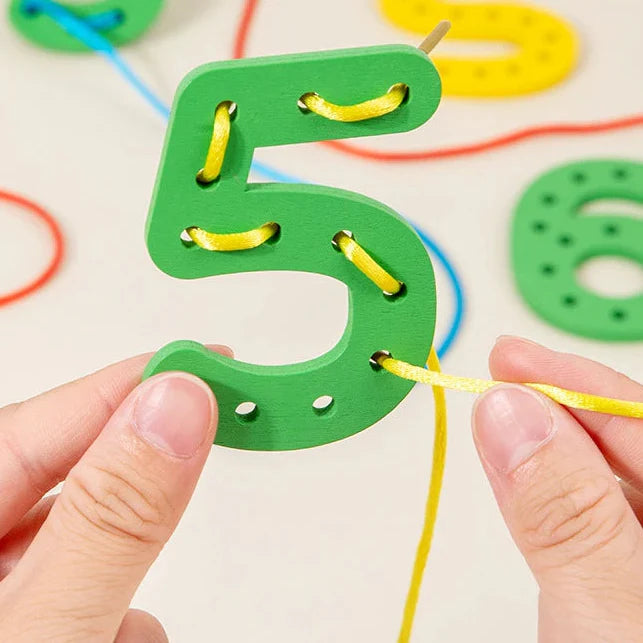 Close-up of a yellow cord threaded through the holes of a green wooden number 5