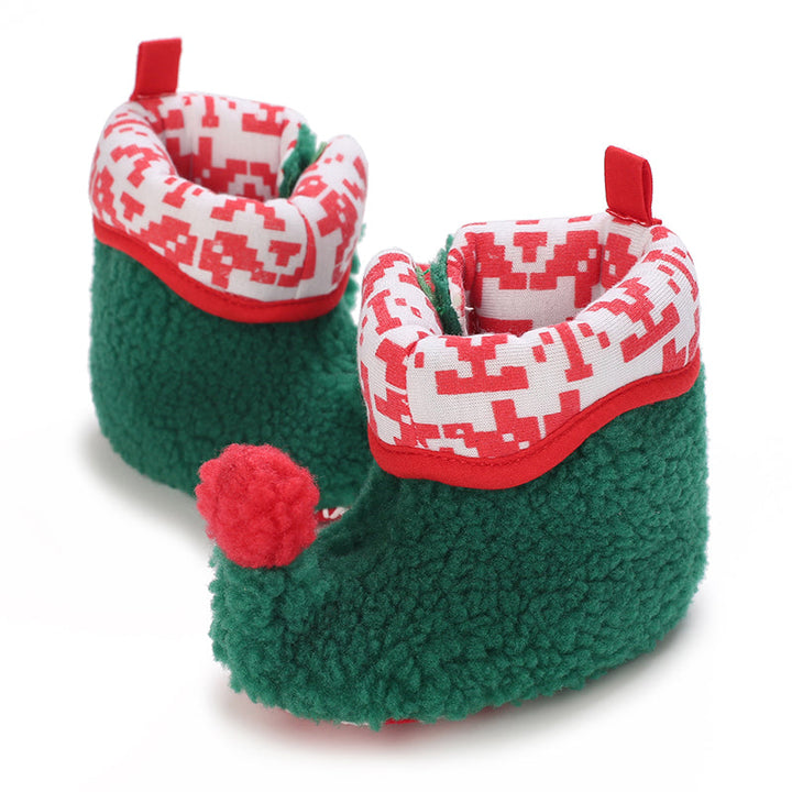 Green plush baby booties with red-and-white patterned cuffs and a red pom-pom