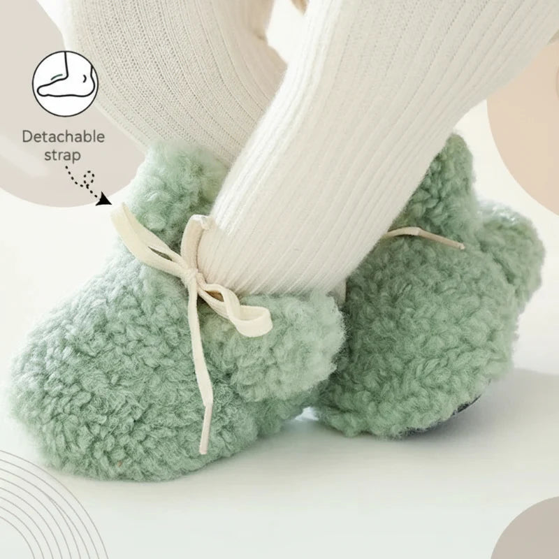 Green plush baby shoes with tied laces and a detachable strap, worn with white socks