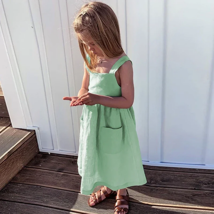 Child wearing the green sleeveless dress with front pockets on a wooden deck