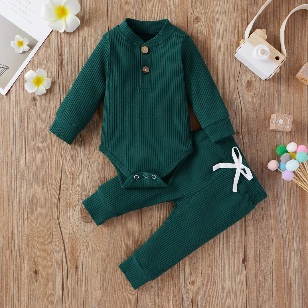 Green ribbed baby bodysuit and matching pants with a white waist tie, arranged on a wooden surface