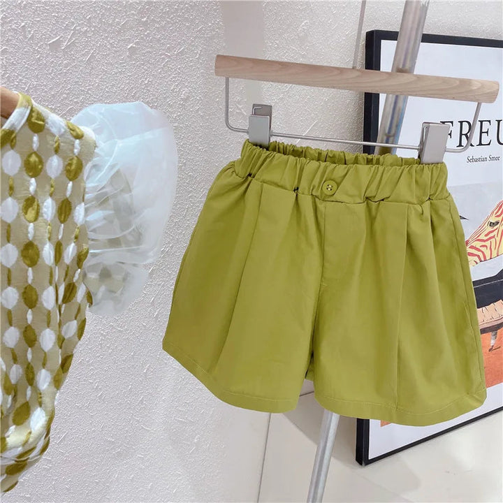 Green shorts with a gathered elastic waistband beside the patterned top