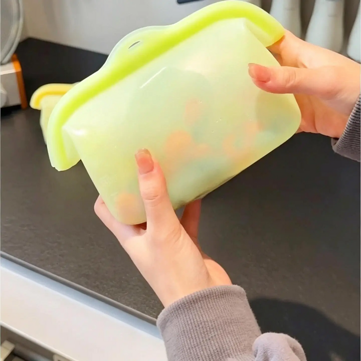 Hands holding a green silicone food storage bag with its top closed.