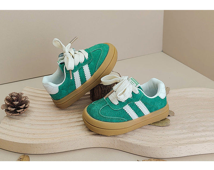 Green low-top sneakers with white laces and side stripes on a wooden display