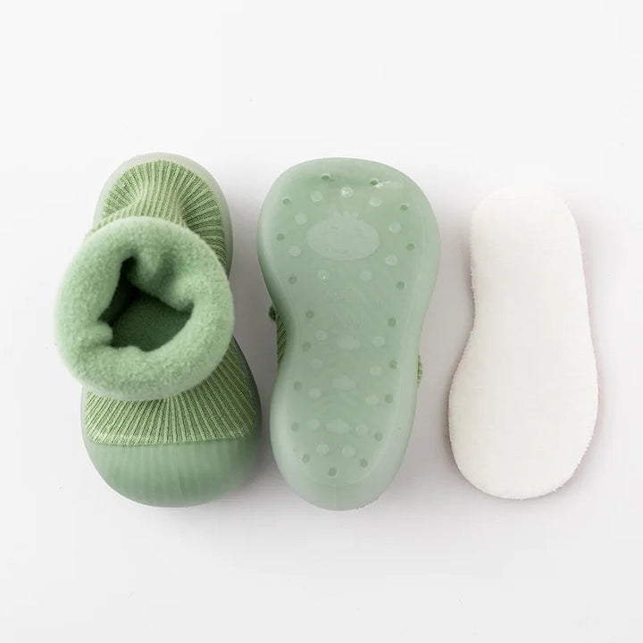 Green sock shoes showing the cuff opening and dotted sole, with a white insole beside them.