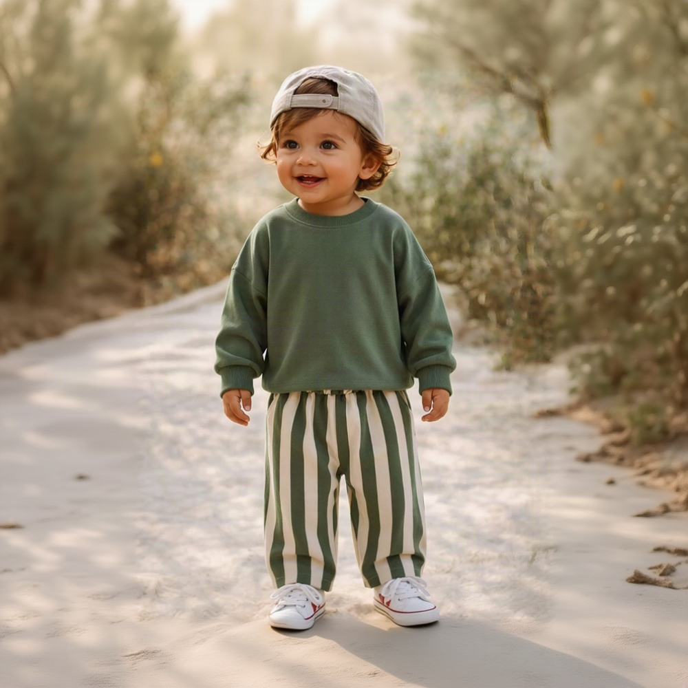Toddler wearing green and cream striped pants with a green sweatshirt outdoors