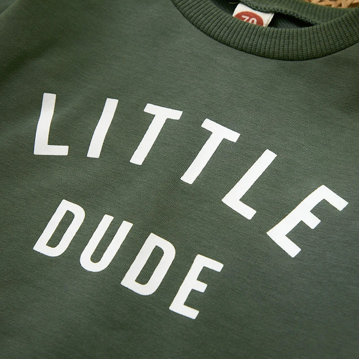 Close-up of white Little Dude lettering and the ribbed neckline on the green sweatshirt