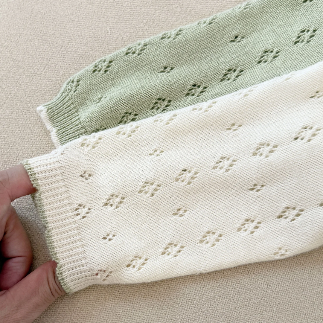 Close-up of green and white knit sleeves with ribbed cuffs and small diamond openings