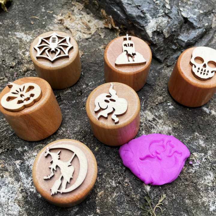 Six Halloween wooden clay stamps with a purple dough impression on a stone surface.