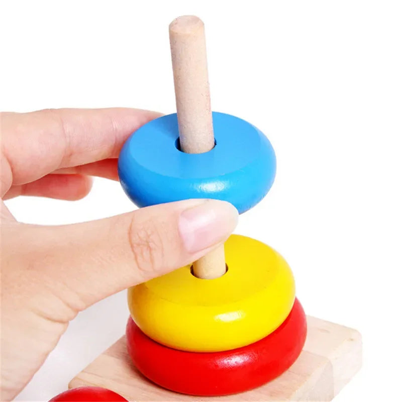 Hand sliding a blue stacking ring onto a wooden post above yellow and red rings