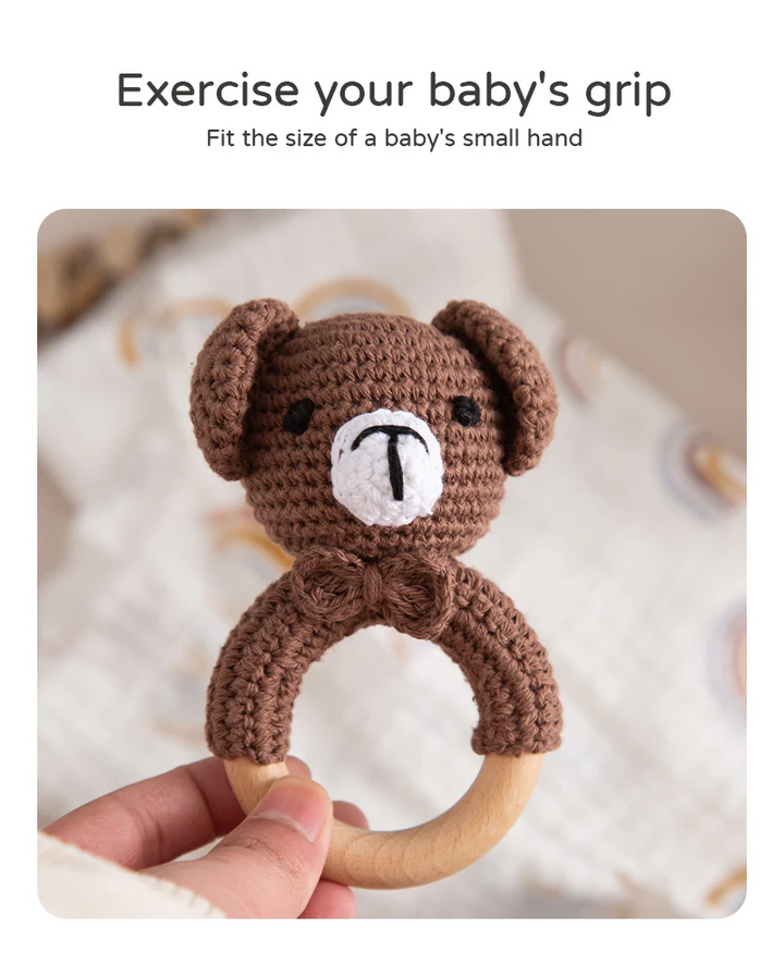 Hand holding a brown bear crochet rattle by its round wooden ring