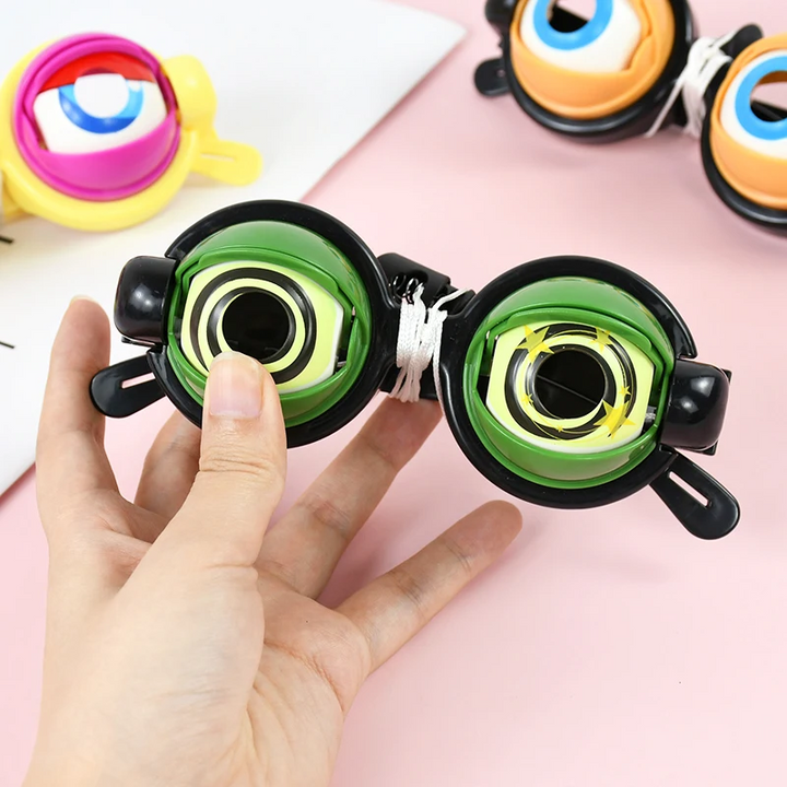 Hand holding green spiral-eye toy glasses beside yellow and black styles
