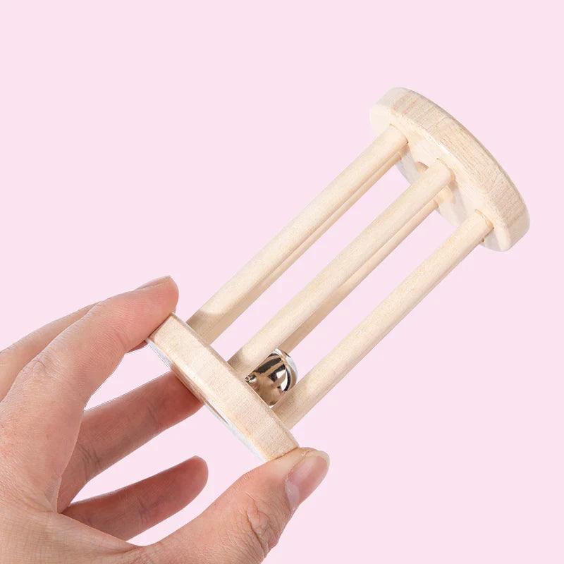 Hand holding a long wooden cage rattle with a silver-colored bell against a pink background
