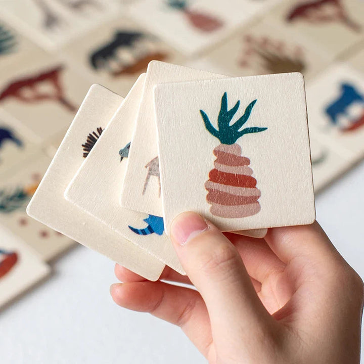 Hand holding wooden matching tiles with a plant design on the front tile