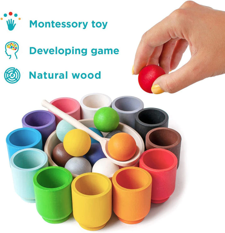 Hand holding a red wooden ball above a color sorting set with cups, bowl, and spoon