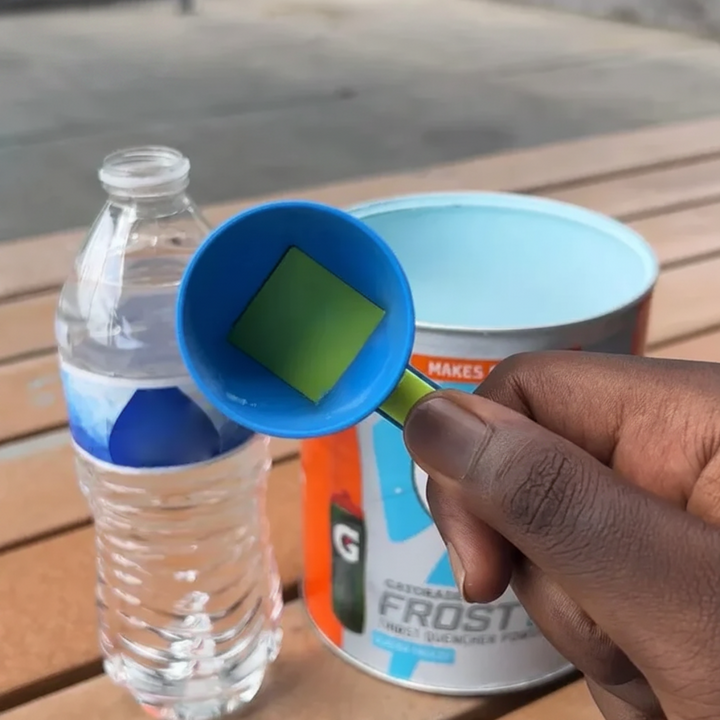 Hand holding a blue measuring scoop beside an open bottle and a powder container