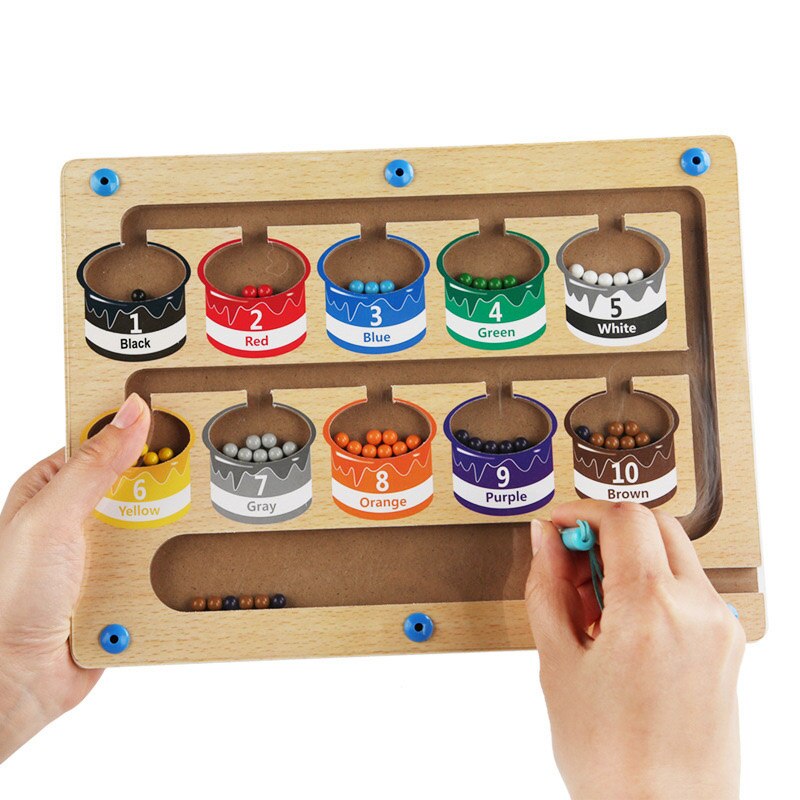 Hands holding a wooden magnetic maze with ten numbered color-sorting cups.