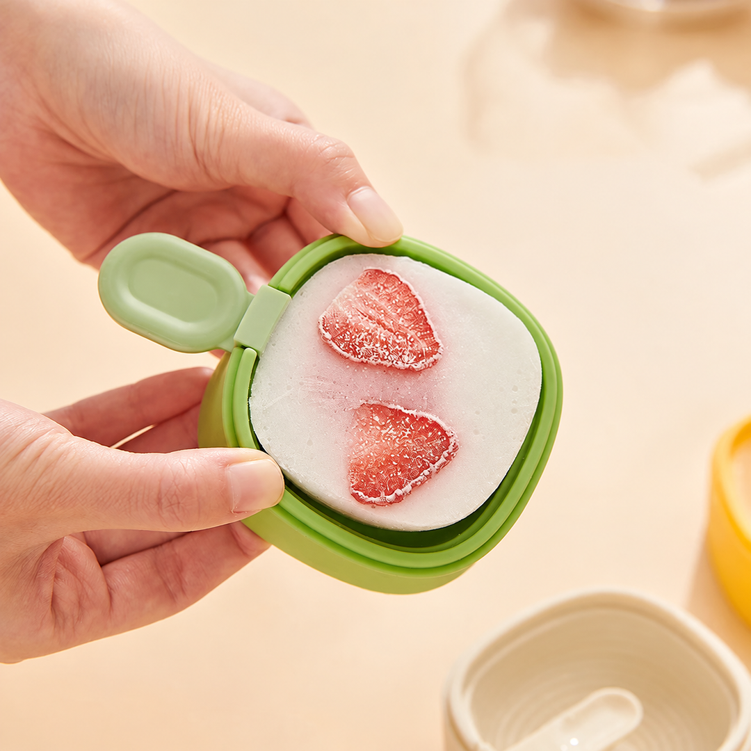 Hands holding a green ice cream mold filled with a frozen treat and strawberry slices.