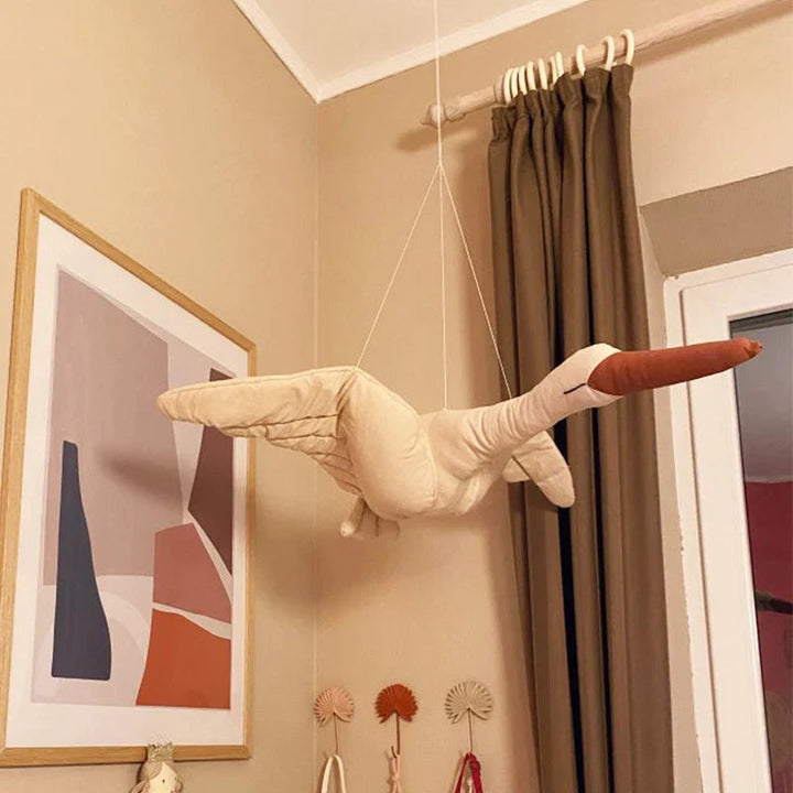 Hanging fabric swan with a rust-colored beak beside framed art and curtains