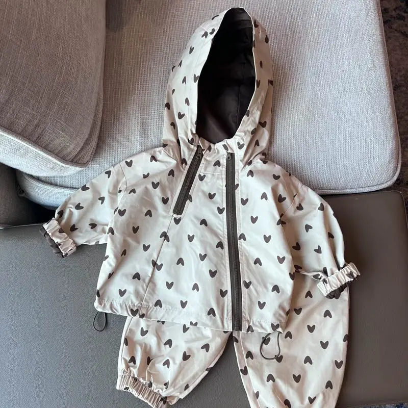 Heart-print hooded jacket and matching pants arranged on a gray armchair.
