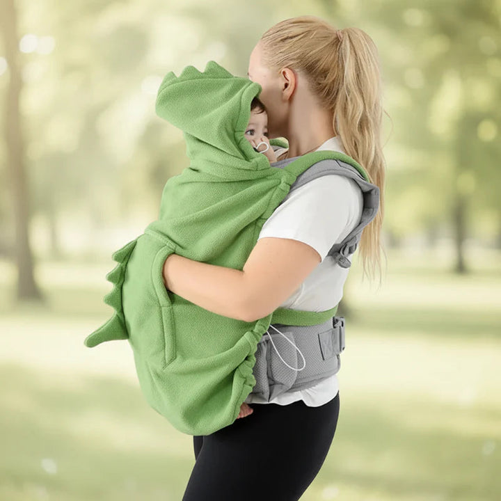Baby facing a parent beneath a green hooded carrier cover with raised dinosaur spikes