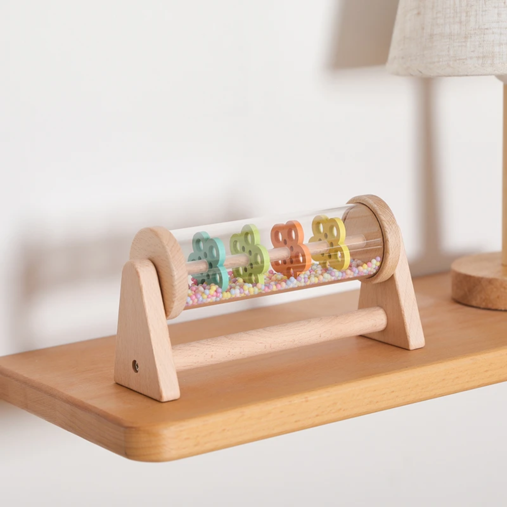 Wooden rain sound toy displayed horizontally on a side table beside a lamp.