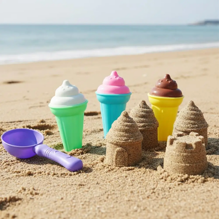 Toy ice cream cones and a purple scoop arranged beside small sandcastles at the beach