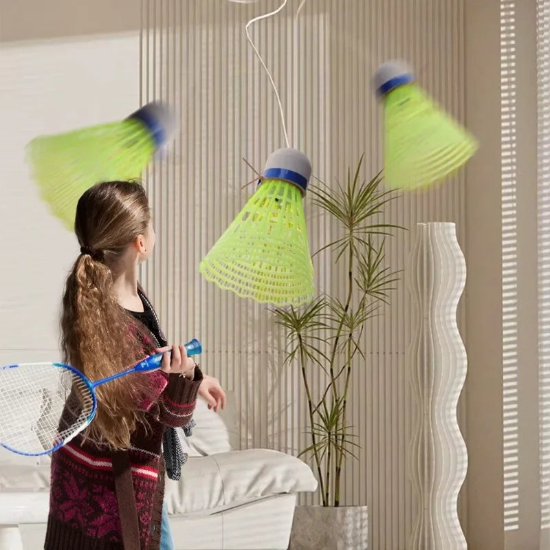 Player practicing indoors with a racket and a suspended green badminton shuttle