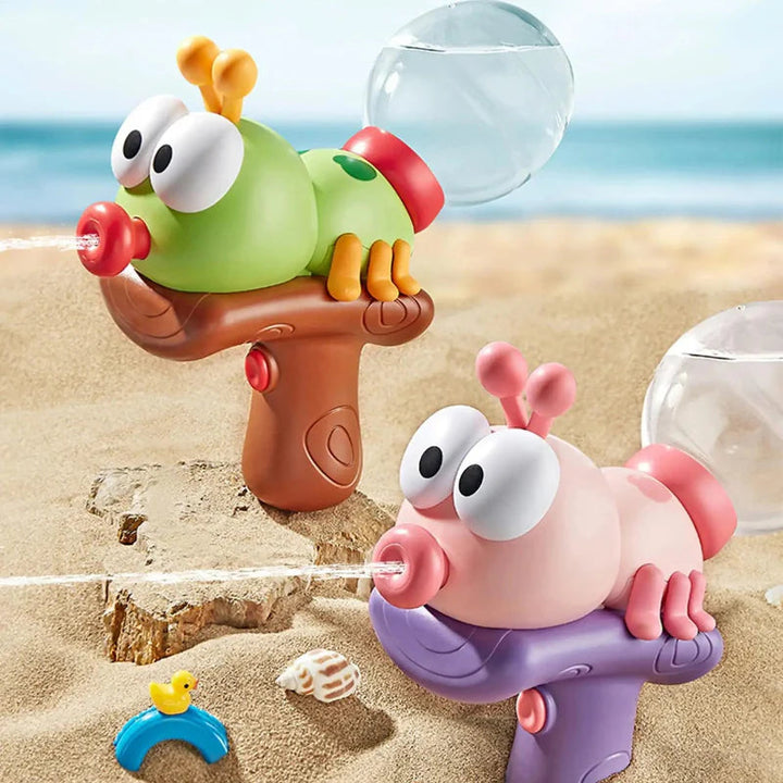 Green-and-brown and pink-and-purple water guns with round transparent reservoirs on beach sand.