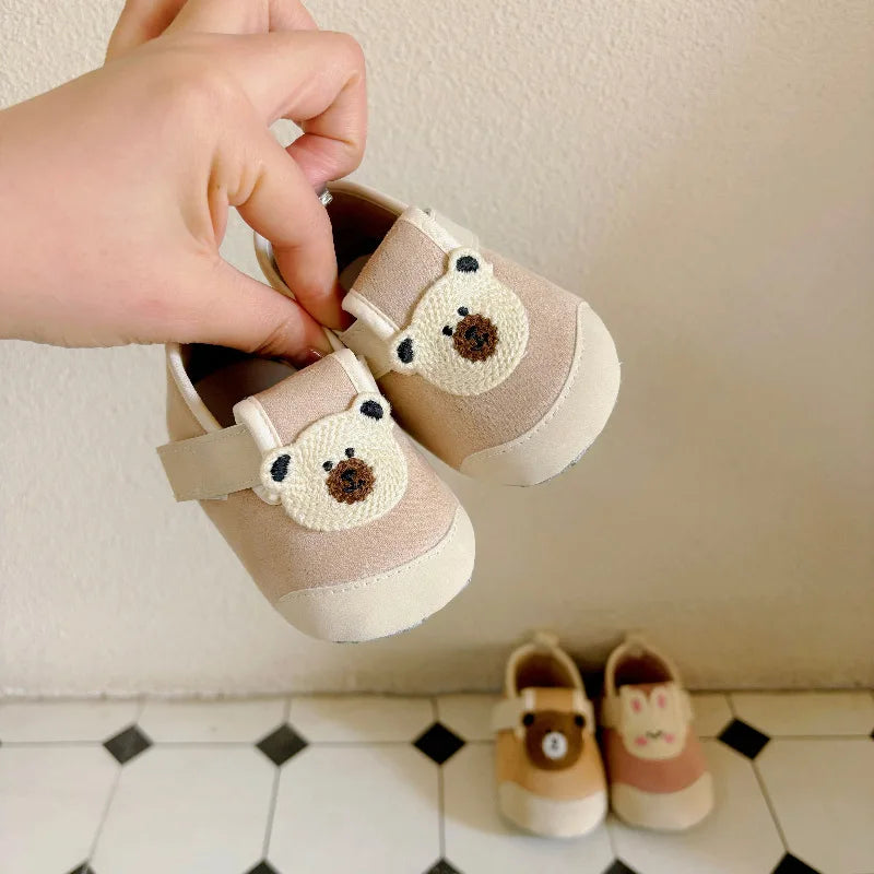 Khaki bear baby shoes held to show their fabric uppers and side straps
