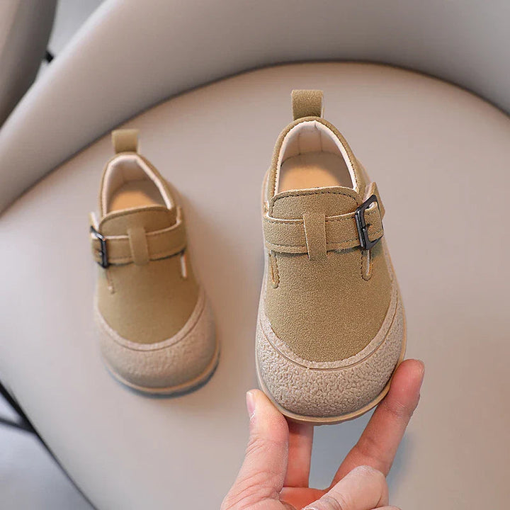 Khaki baby shoes with rounded toes and buckle details, one held up for a front view