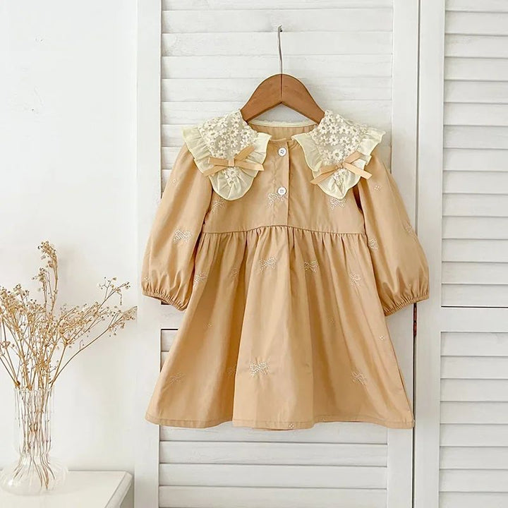 Khaki dress with a cream lace collar, gathered sleeves, and flared skirt against white shutters
