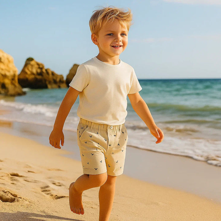 Child walking on a beach in khaki dinosaur-print shorts and a white T-shirt
