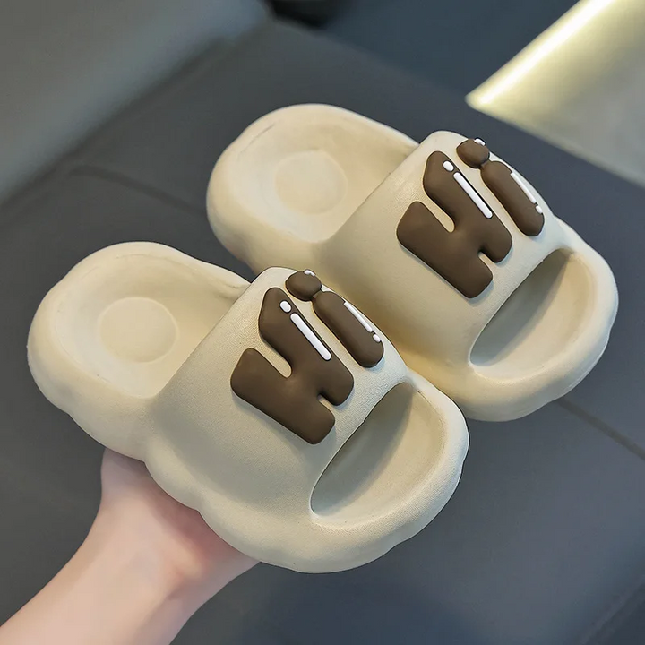 Khaki slide slippers with raised brown Hi lettering.