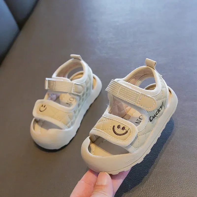 Khaki sandals on a dark tabletop, showing the front straps and open toes.