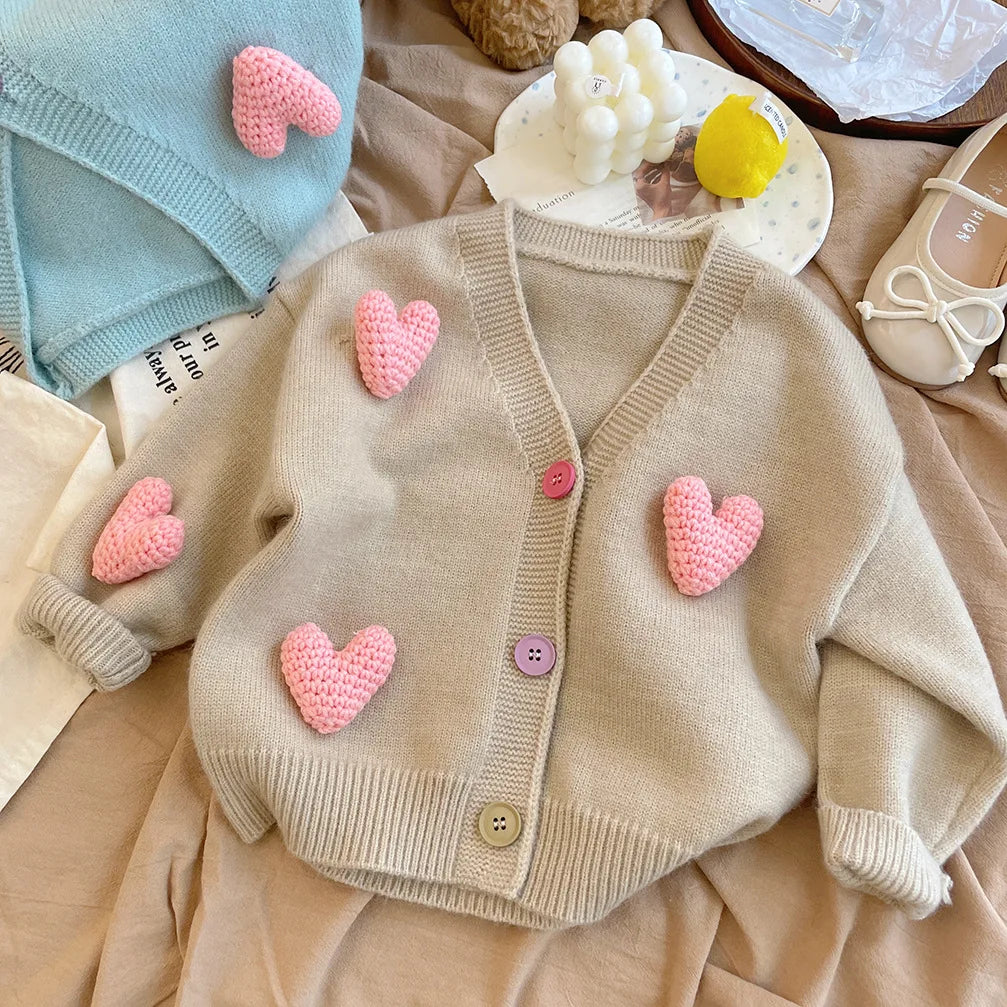 Khaki knit cardigan on bedding with raised pink hearts and contrasting buttons