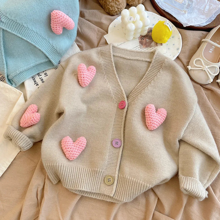Khaki knit cardigan on bedding with raised pink hearts and contrasting buttons