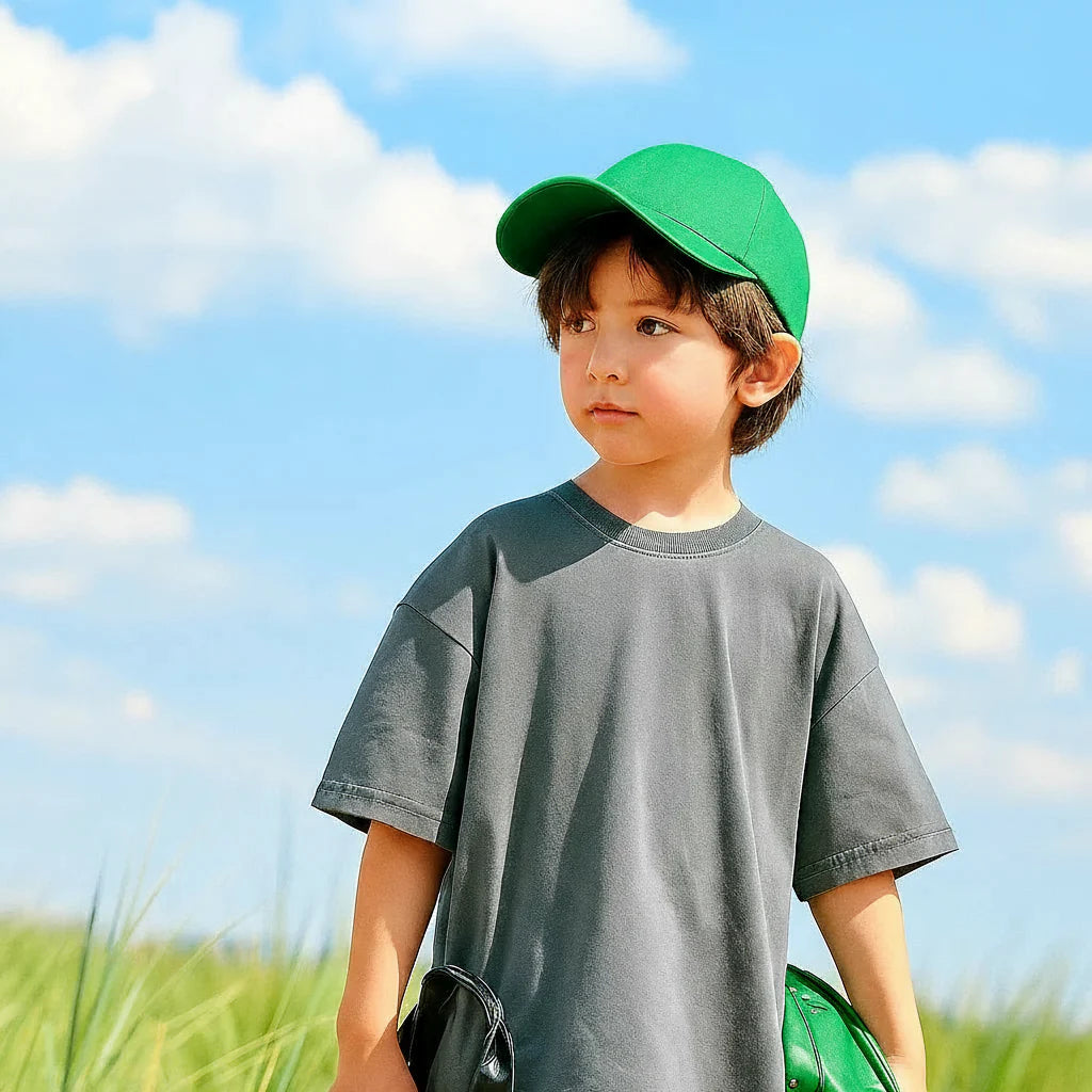 Child wearing a relaxed dark gray T-shirt and green cap outdoors