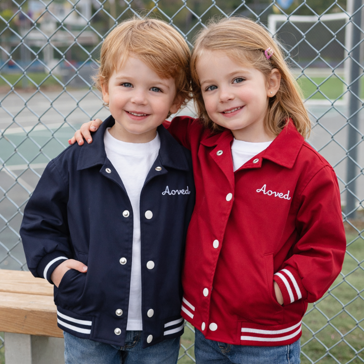 Two children wearing blue and red baseball jackets with striped trim and front pockets outdoors
