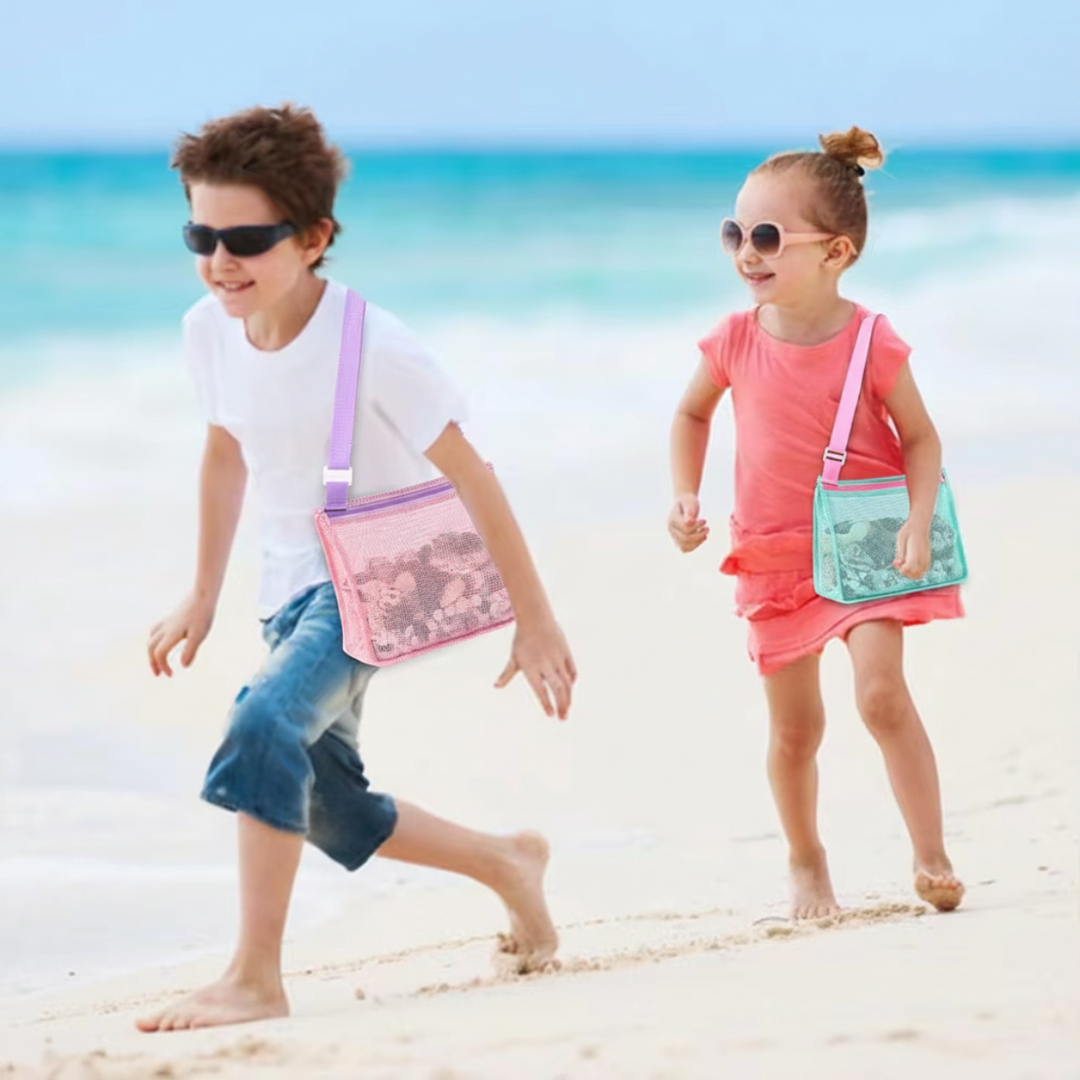 Two children running along the shore with pink and mint mesh shoulder bags