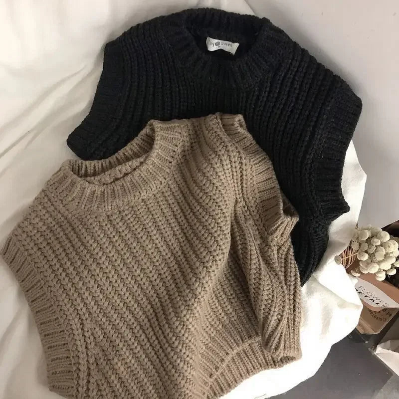 Brown kids' sweater vest arranged in front of a black vest on light fabric