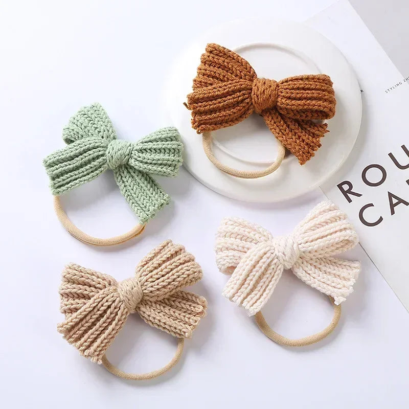 Four knitted bow headbands in green, rust, beige, and cream arranged on a white surface