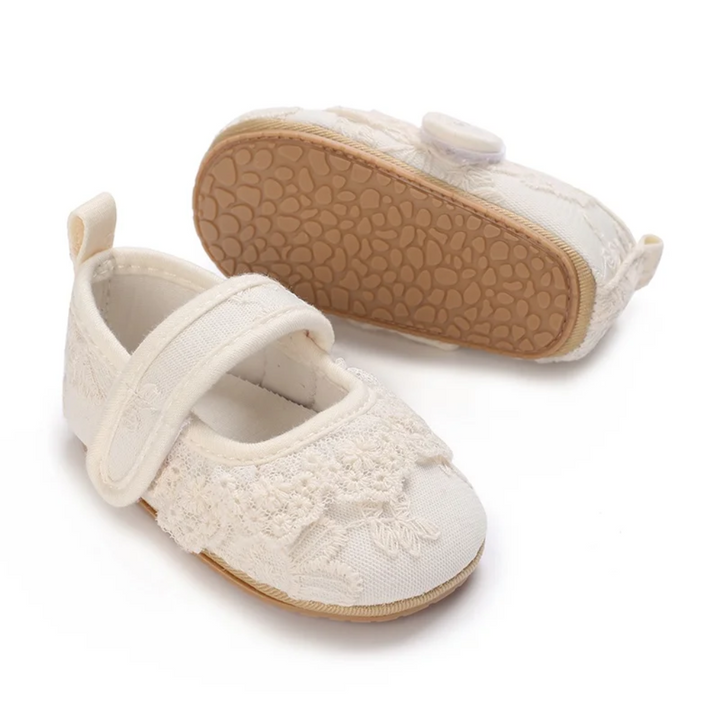 White lace baby shoes with a tan patterned rubber outsole shown