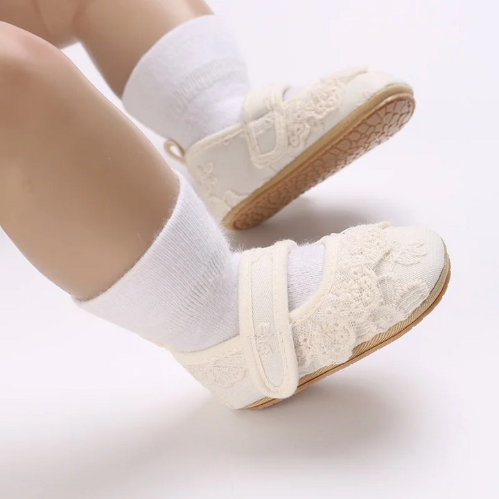 White lace baby shoes worn with white socks, viewed from the side